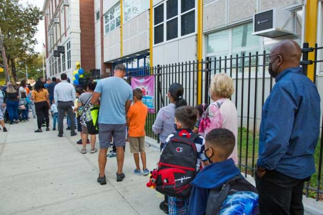 Groups of parents and students are lined up waiting for the school doors to open.