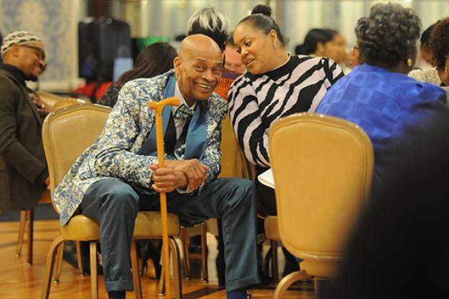 A man with a cane listens to what the woman on the right of him is saying