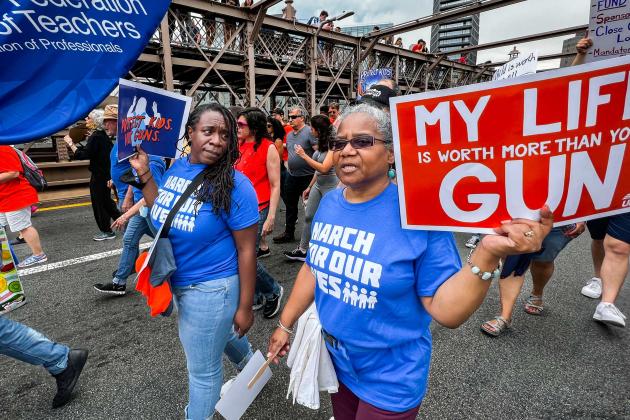 Two women walk across a bridge holding signs with a group