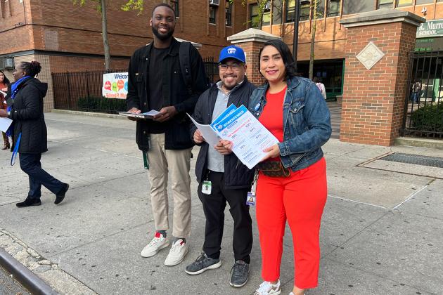 A group of staff members are outside of their school building ready to hand out fliers. 