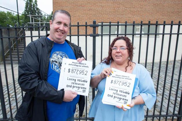 A man and woman hold signs and smile