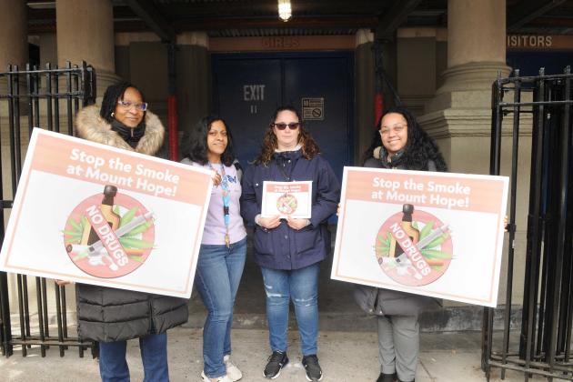 4 woman pose outside of a school building with signs that say "Stop the Smoke"