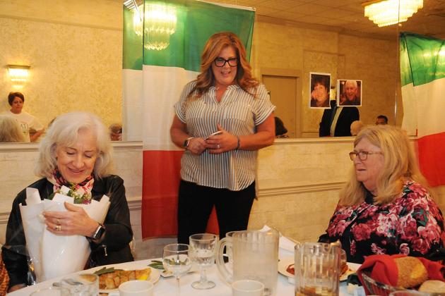 A woman in the middle presents the two women who are seated with flowers in honor of their late sister. 