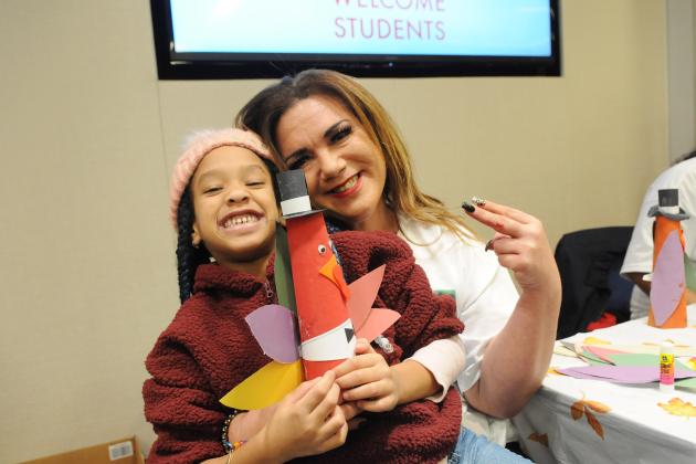 A woman and student pose for a photo showing off a paper turkey