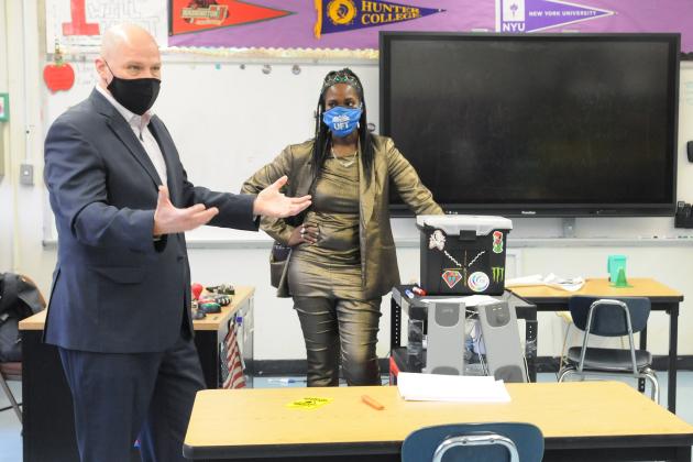 UFT President talking while moving his hands. Woman in the background observes. Both are wearing masks, 