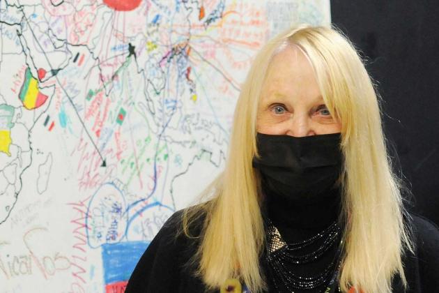 A woman poses in front of a drawing of a map 