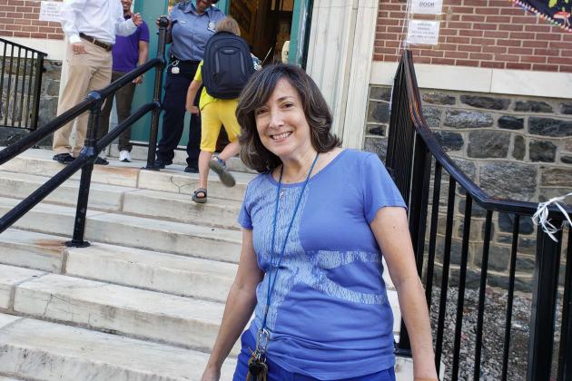 A teacher smiles outside a school building