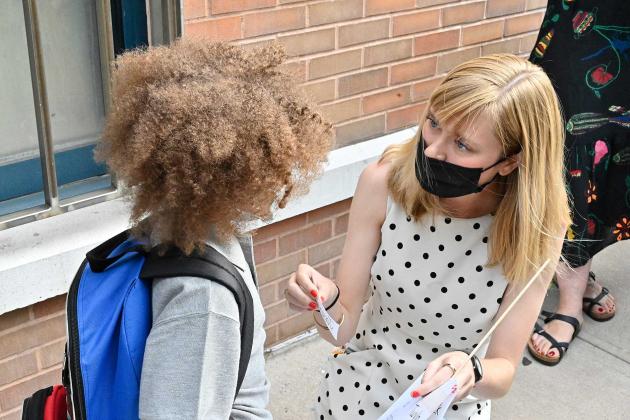 A teacher on the right gives a nametag to her student. 