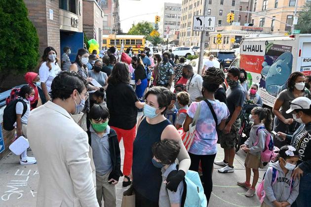 A large group of parents and students waiting outside to get into the school building. 
