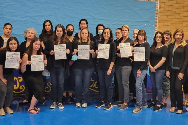 A group of staff members wearing black pose and hold up signs protesting budget cuts.