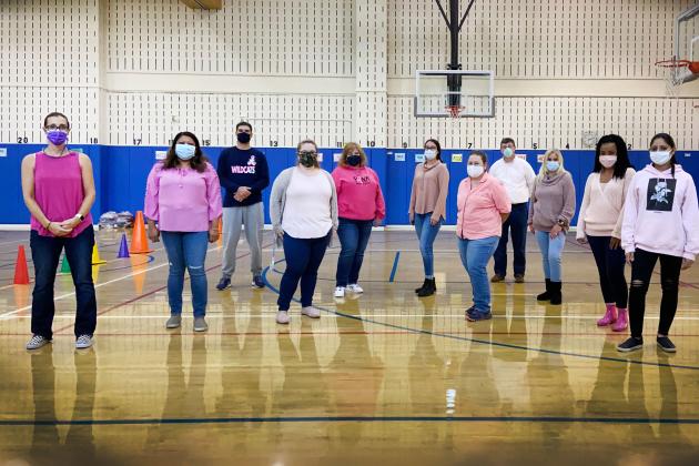A large number of staff members get together for a photo in the basketball gym.