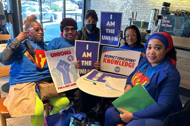 A group of members pose at a table holding their signs for the day of action
