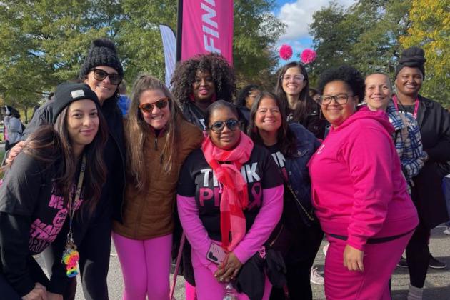 A group of marchers pose while wearing pink breast cancer awareness attire 
