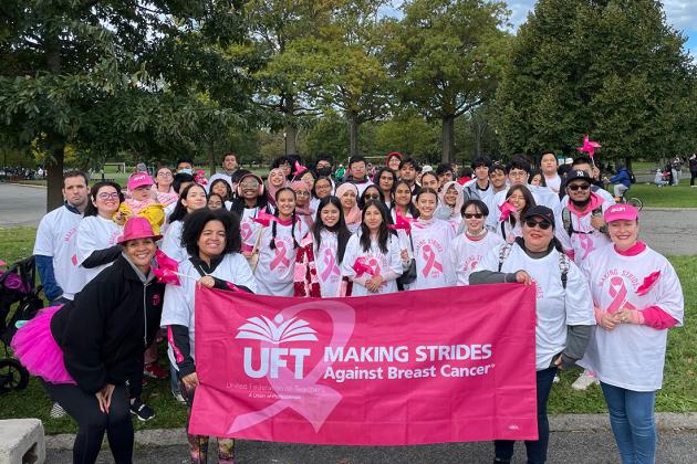 A large group of marchers take a photo with a pink banner in front of them