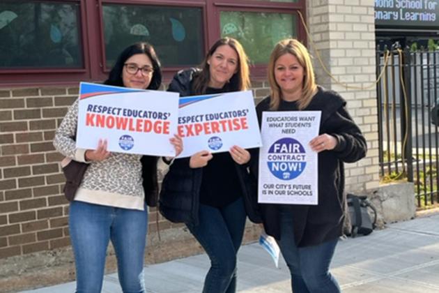 Three women hold up signs 