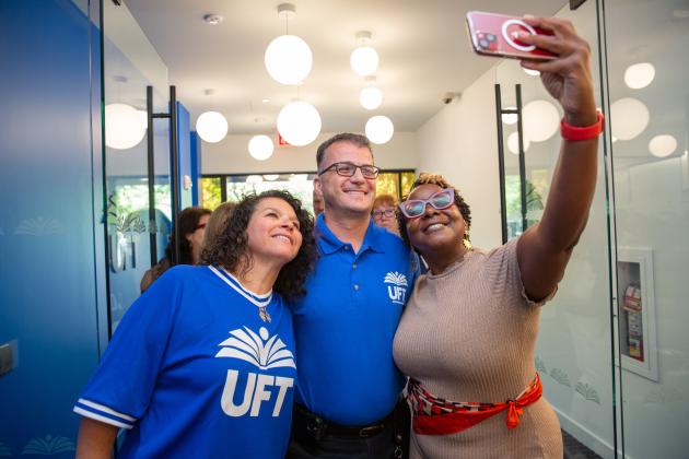 Three people smile while the woman on the right takes a selfie of them.