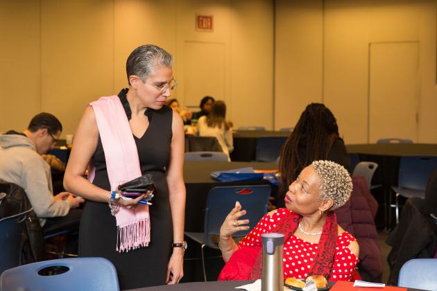 Two women engage in a conversation at a table. The woman on the right is explaining something. 