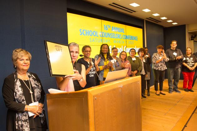 A group of members stand at the podium honoring the former counselor chapter leader on the left