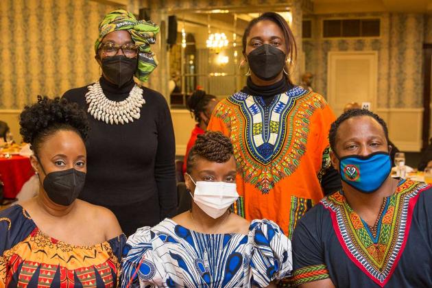 5 people all wearing masks pose for a group photo at a table. 