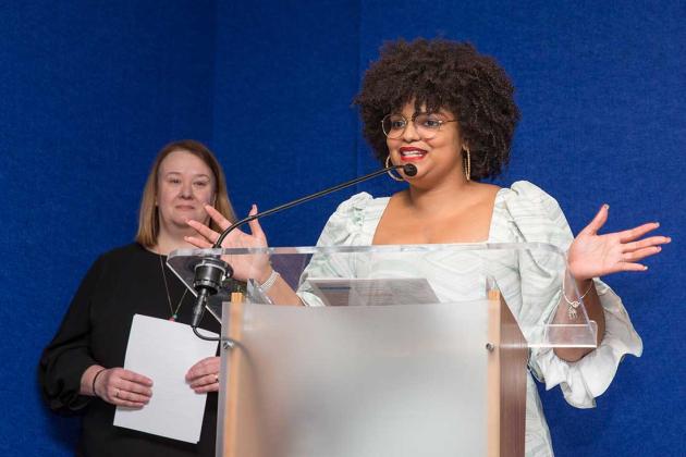 A woman speaks at the podium with her hands stretched outward