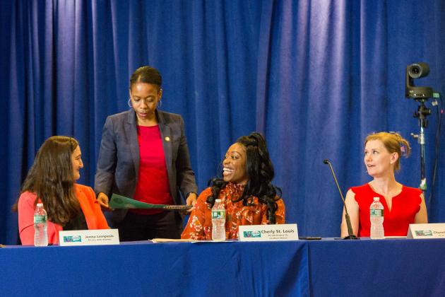 A woman stands at a table and looks at three women sitting at the table