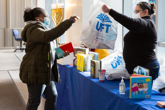 One woman is handed a bag of books by another woman behind a table. 