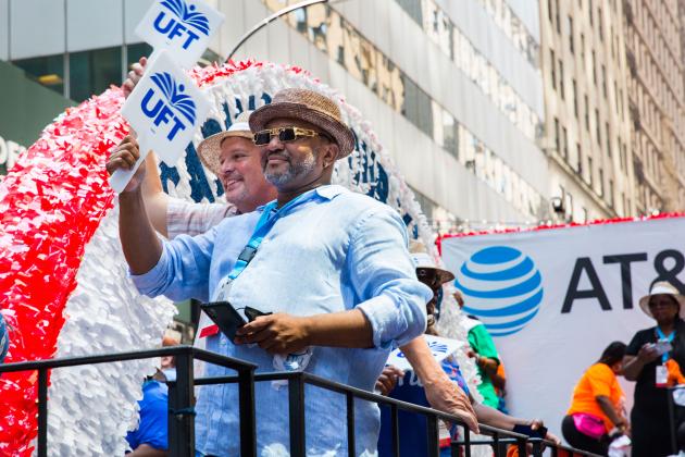 Two men on the float, both wearing fedora hats and one wearing sunglasses, smiling on the float. 