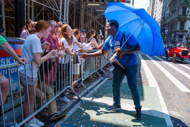 A man walking in the parade greets people cheering by the sidewalk. 