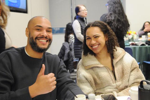 A social worker on the left flashes a "thumbs up" as the social worker next to him smiles. The two social workers are seated at a table during the 2026 UFT Clinicians Appreciation Day event. 
