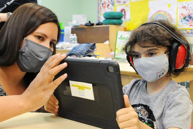Teacher Melissa Curto works with a student, wearing headphones to block noise, as he completes a math lesson in her self-contained classroom at PS 45 on Staten Island.