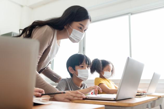 An adult and two students wearing masks, looking at computers