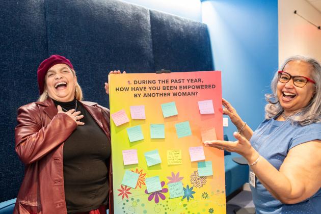 Two UFT members at the UFT HERstory brunch take a photo holding a sign advocating for women's empowerment. 