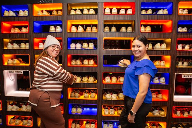 Two colleagues at a new member event take a picture at a bowling alley by the  rental shoes. 