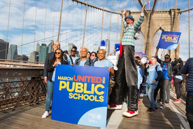 Marchers hold signs on Brooklyn Bridge including man on stilts