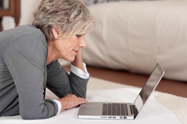 Mature woman laying on the floor looking at her laptop