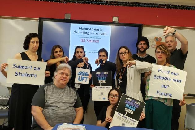 A group of union members have their hands in a "thumbs down" gesture. Some hold posters that say "support our students", "fund our schools and our future", and "our kids need small class sizes."