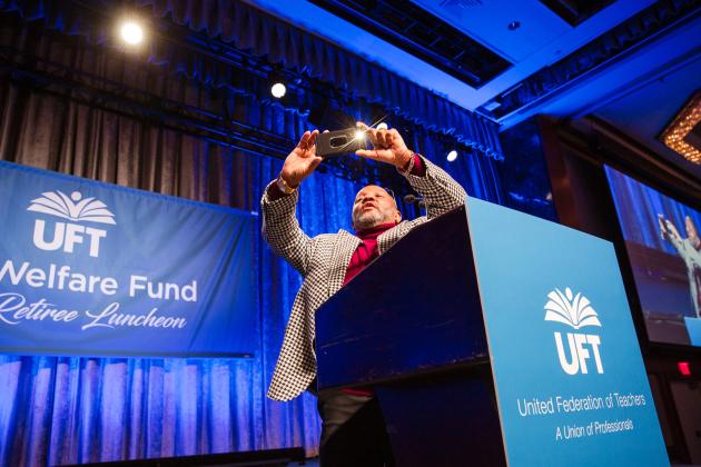 Luncheon emcee Anthony Harmon takes a selfie on stage as he encourages retirees to share their photos on social media at the UFT New Retiree Luncheon on Dec. 5, 2024. 