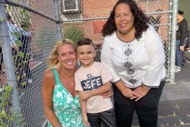 A student and two teachers stand outside a school building