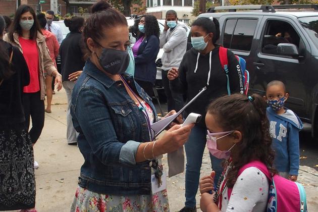 Teacher with thermometer stands outside of school with student