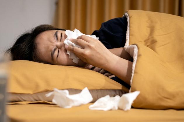 Women in bed blowing nose under a yellow blanket