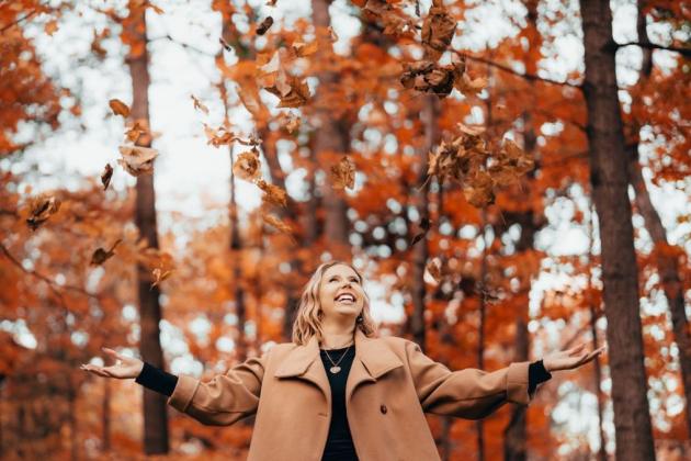 woman-smiling-with-arms-open-as-leaves-fall-in-autumn-forest