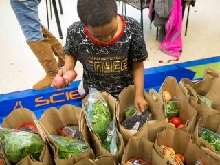 A student tops off a grocery bag with raw beans and potatoes.