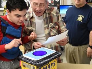 Paraprofessional Bill Boyle helps Joseph work with a communication device while 