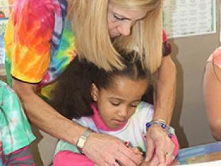 Teacher Nancy Bishop helps a 1st-grader with her handprint.