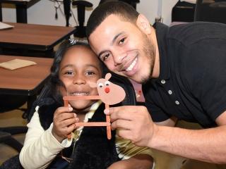 A PS 5 student proudly shows the reindeer she made to Lawrence Gonzalez, a teach