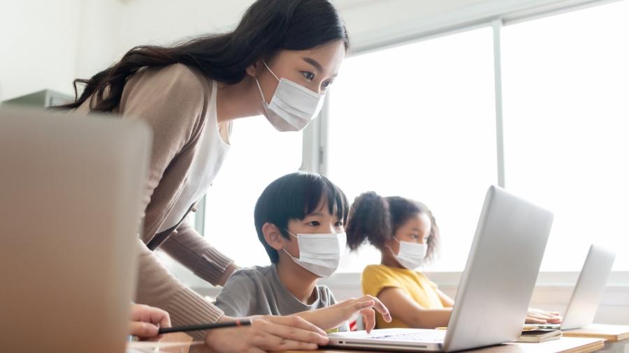 An adult and two students wearing masks, looking at computers