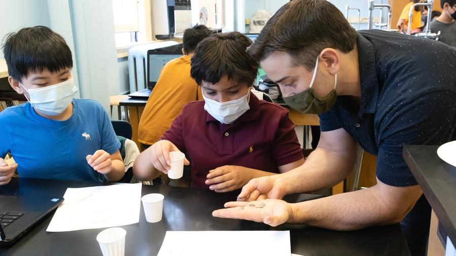 Jon Carrai, a history teacher at IS 187 in Brooklyn, examines the symbols on ancient Roman coins with two of his 6th-graders. 