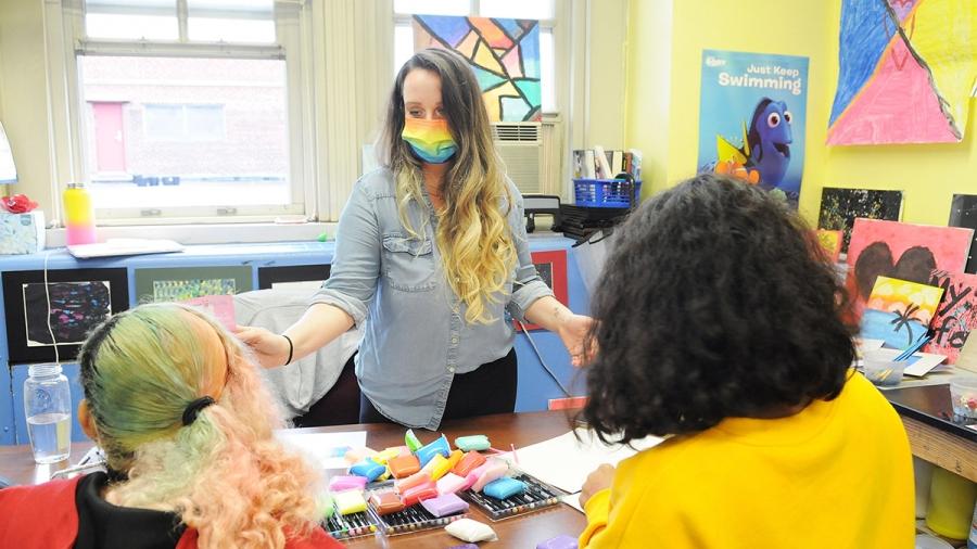 Educator wearing a rainbow mask demonstrates for two students