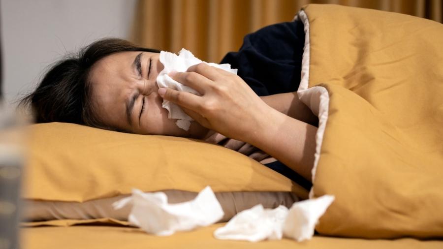 Women in bed blowing nose under a yellow blanket