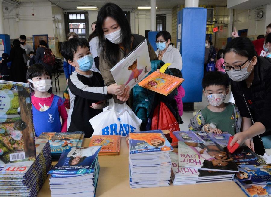 Two parents wearing masks go through a selection of books with their children, also wearing masks. 